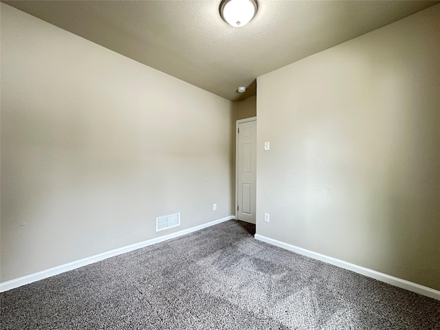 empty room featuring baseboards, dark carpet, and visible vents