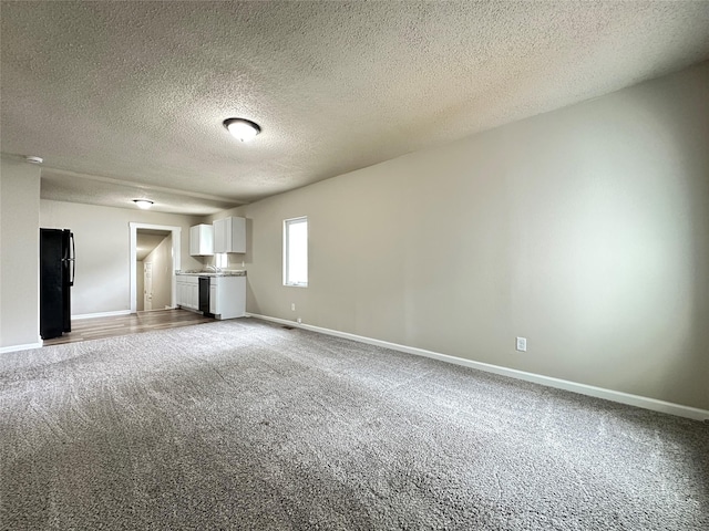 unfurnished living room with carpet flooring, a textured ceiling, and baseboards