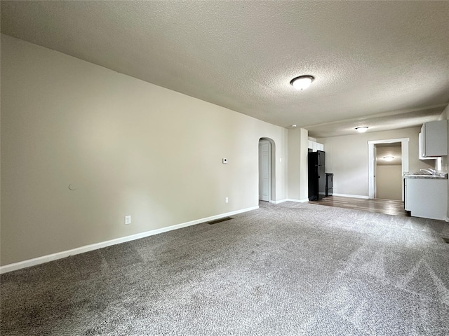 unfurnished living room with arched walkways, a textured ceiling, dark carpet, baseboards, and visible vents