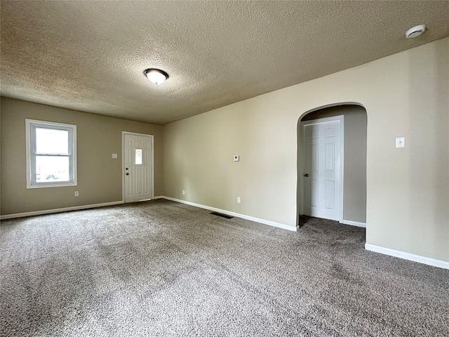 spare room with carpet flooring, arched walkways, a textured ceiling, baseboards, and visible vents