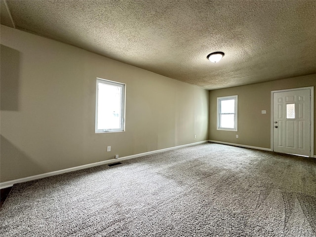 carpeted empty room with baseboards, a textured ceiling, and visible vents