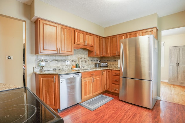 kitchen with appliances with stainless steel finishes, light stone counters, a sink, light wood-style flooring, and backsplash