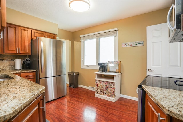 kitchen with brown cabinets, light stone countertops, appliances with stainless steel finishes, baseboards, and dark wood-type flooring