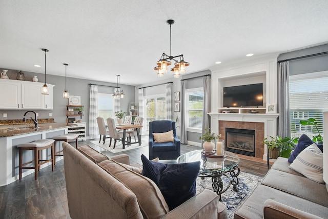 living room featuring dark wood-style flooring, baseboards, recessed lighting, a tile fireplace, and a notable chandelier