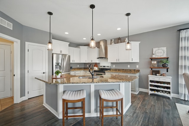 kitchen with wall chimney range hood, a sink, stainless steel appliances, white cabinetry, and visible vents