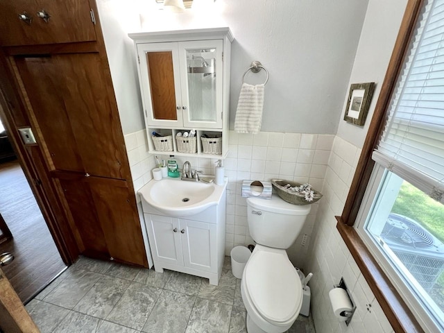 bathroom with toilet, tile walls, wainscoting, and vanity
