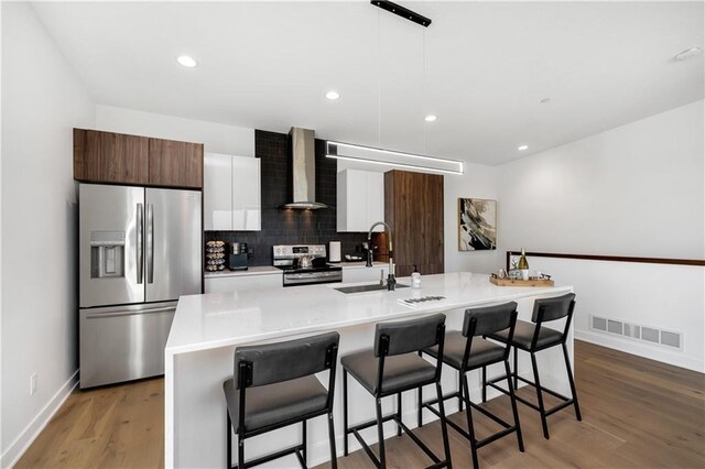 508 Indianola Rd Unit 1, Des Moines, IA 50315 - kitchen featuring wall chimney range hood, appliances with stainless steel finishes, light countertops, a breakfast bar area, and visible vents