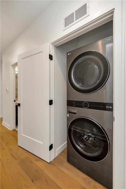 508 Indianola Rd Unit 1, Des Moines, IA 50315 - clothes washing area featuring laundry area, visible vents, stacked washing maching and dryer, baseboards, and light wood-style flooring