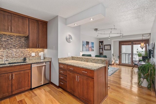 kitchen with backsplash, stainless steel dishwasher, a sink, light wood finished floors, and a peninsula