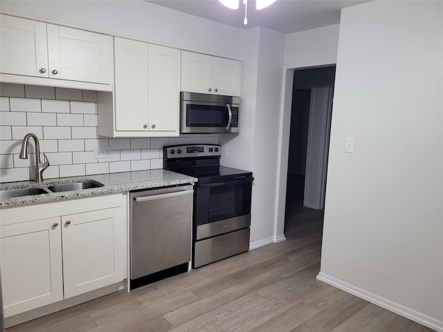 kitchen with white cabinets, a sink, light wood finished floors, stainless steel appliances, and backsplash