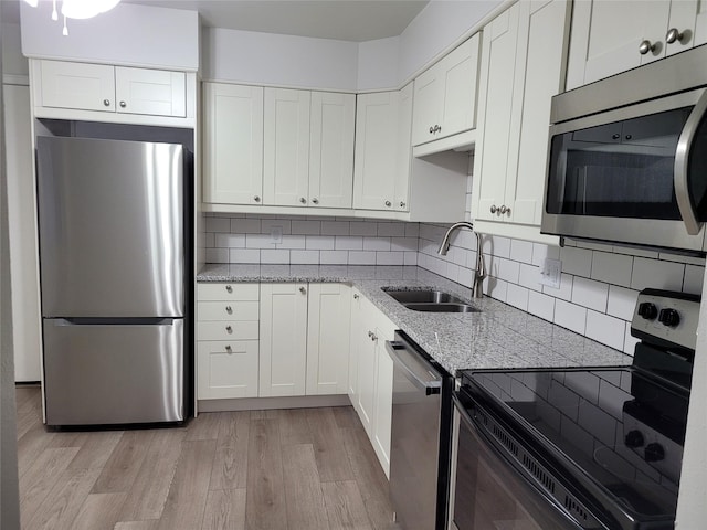 kitchen featuring white cabinetry, light stone counters, a sink, light wood finished floors, and stainless steel appliances