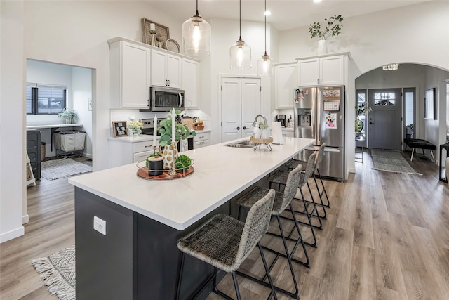 kitchen featuring a high ceiling, arched walkways, white cabinets, a sink, and appliances with stainless steel finishes