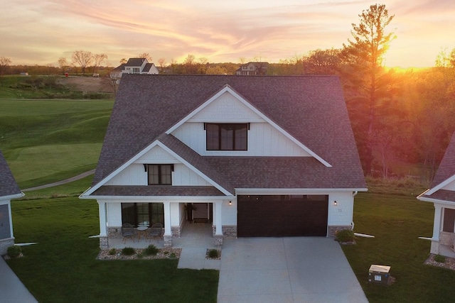 view of front of home with a lawn, a shingled roof, stone siding, and concrete driveway