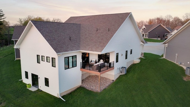 back of property at dusk featuring a yard, central AC unit, and roof with shingles