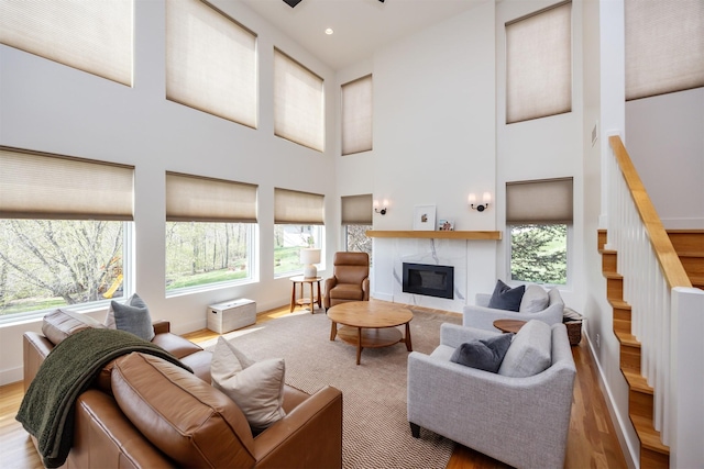 living area featuring a towering ceiling, wood finished floors, a wealth of natural light, and a fireplace
