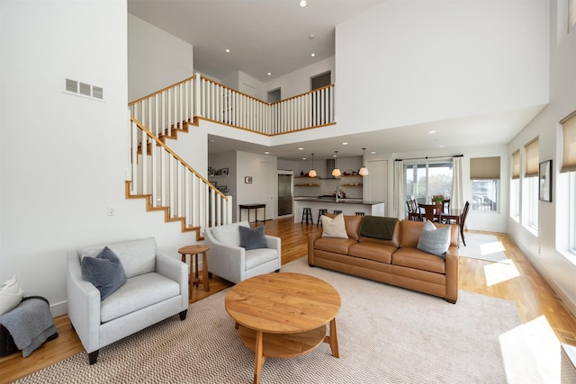 living room with light wood-style flooring, stairs, recessed lighting, a towering ceiling, and visible vents