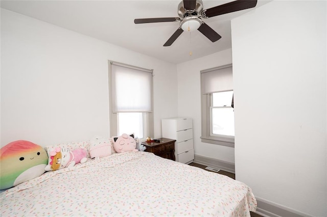 bedroom featuring a ceiling fan, baseboards, multiple windows, and wood finished floors