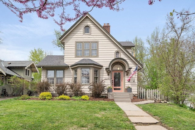 view of front of home with fence, a chimney, a shingled roof, and a front yard