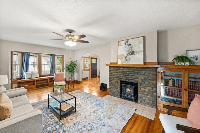 living area featuring arched walkways, a ceiling fan, wood finished floors, and a wood stove