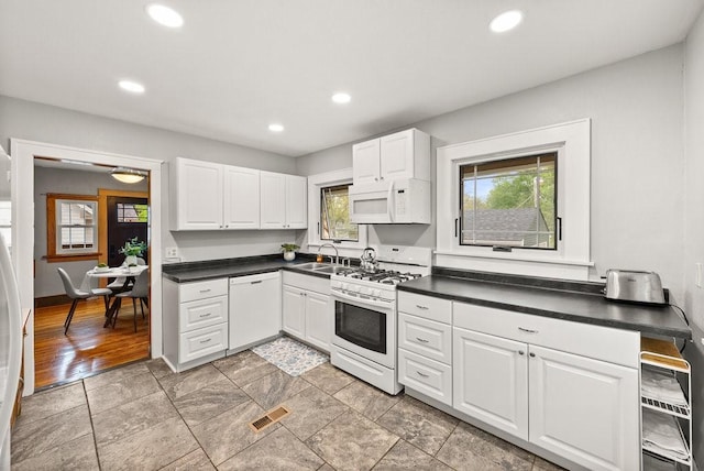 kitchen with dark countertops, a sink, white appliances, recessed lighting, and visible vents