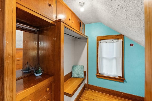 mudroom featuring a textured ceiling, baseboards, light wood-style flooring, and lofted ceiling
