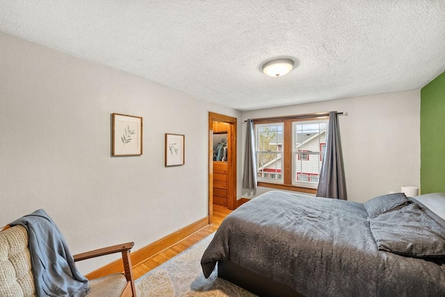 bedroom with a textured ceiling, baseboards, and wood finished floors