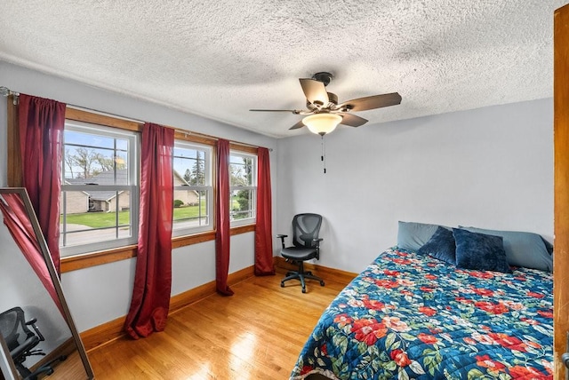 bedroom featuring a textured ceiling, baseboards, a ceiling fan, and light wood finished floors