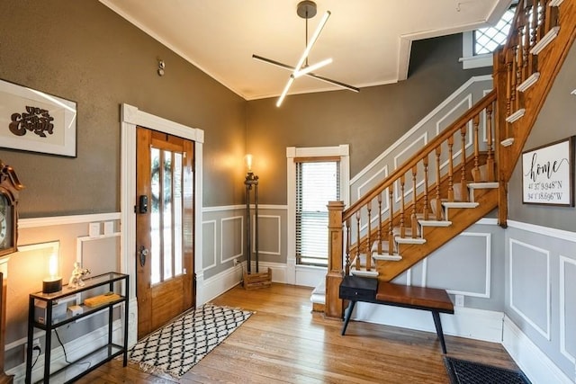 foyer featuring wood finished floors, stairs, a decorative wall, and a wainscoted wall