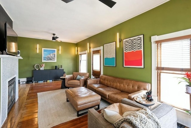 living room with visible vents, a glass covered fireplace, ceiling fan, and wood finished floors