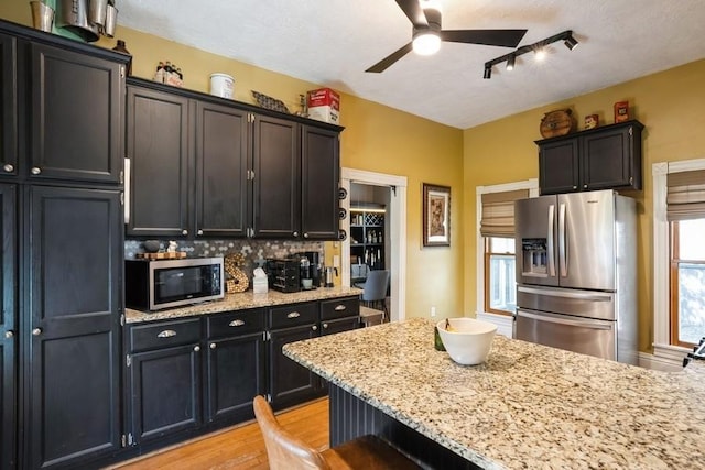 kitchen with a ceiling fan, appliances with stainless steel finishes, tasteful backsplash, light stone countertops, and light wood finished floors