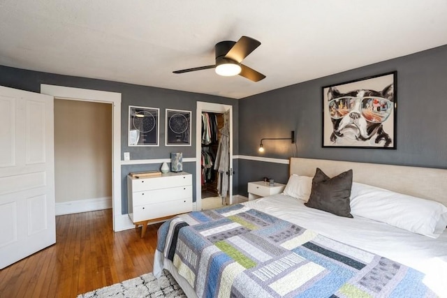 bedroom featuring a walk in closet, ceiling fan, baseboards, wood-type flooring, and a closet