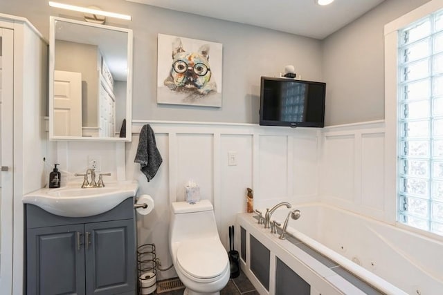 full bathroom with vanity, a wainscoted wall, a whirlpool tub, toilet, and a decorative wall