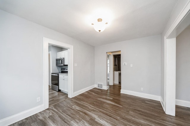 spare room featuring baseboards, dark wood-style flooring, and visible vents
