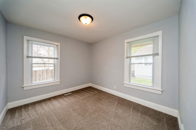 spare room with baseboards, visible vents, and dark colored carpet