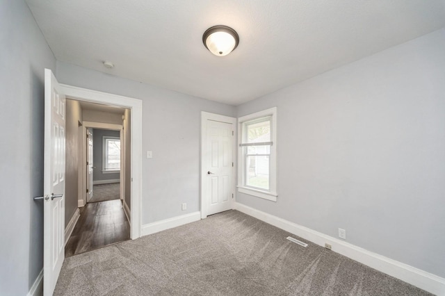 unfurnished bedroom featuring carpet floors, baseboards, multiple windows, and visible vents