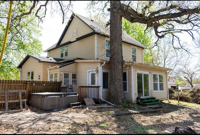 rear view of property featuring a hot tub, fence, and entry steps