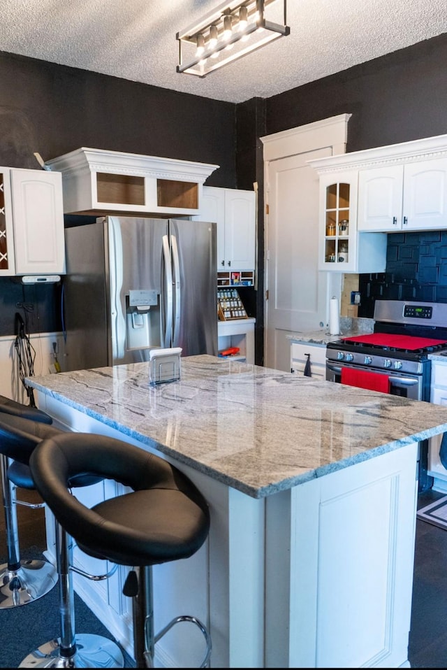kitchen featuring glass insert cabinets, a kitchen breakfast bar, white cabinetry, light stone counters, and stainless steel appliances