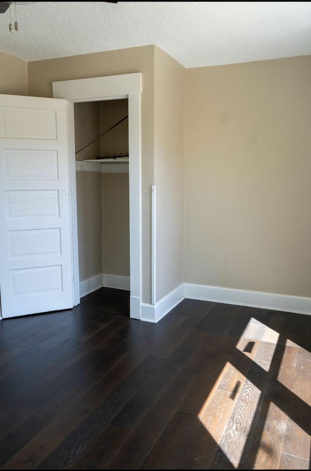 unfurnished bedroom featuring baseboards, a textured ceiling, dark wood-style floors, and a closet