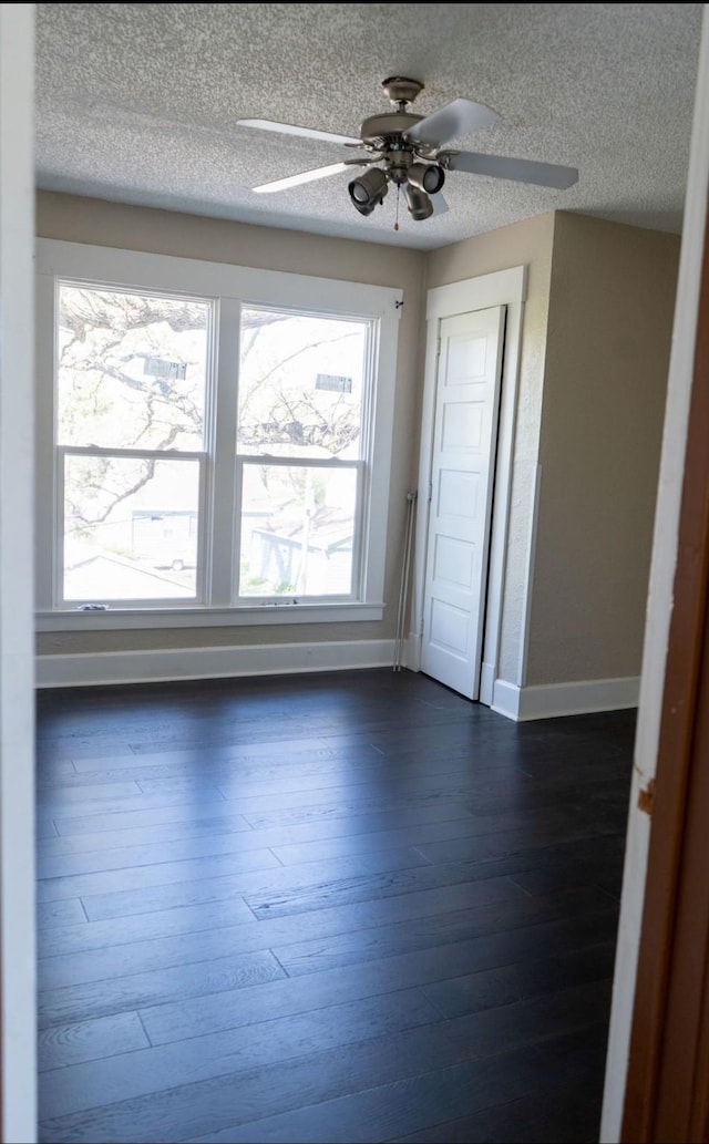 spare room featuring baseboards, ceiling fan, dark wood finished floors, and a textured ceiling