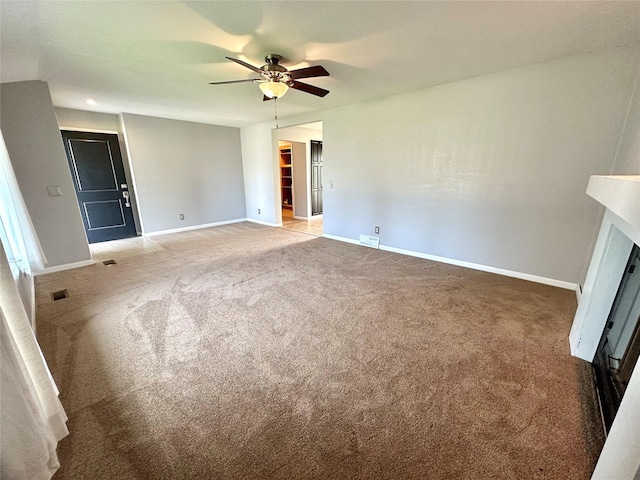 spare room featuring a glass covered fireplace, baseboards, a ceiling fan, and light colored carpet