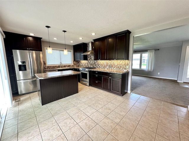 kitchen with backsplash, appliances with stainless steel finishes, a sink, light tile patterned floors, and wall chimney exhaust hood
