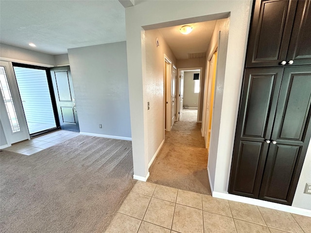 corridor with baseboards, light tile patterned flooring, and light carpet