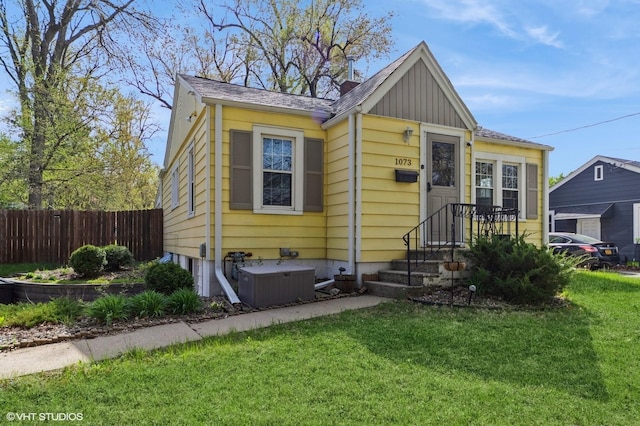 bungalow-style house featuring fence, central AC unit, board and batten siding, and a front lawn