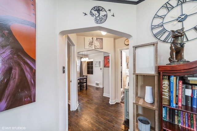 hallway with arched walkways, baseboards, visible vents, and wood finished floors