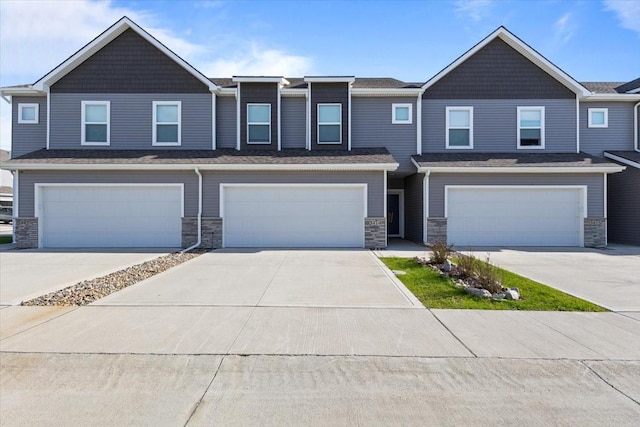 townhome / multi-family property featuring driveway, stone siding, and a garage