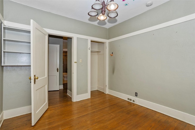 unfurnished bedroom with an inviting chandelier, baseboards, and wood finished floors