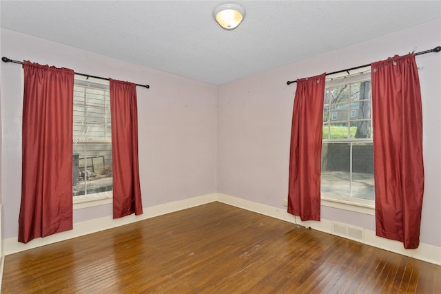unfurnished room featuring visible vents, a textured ceiling, baseboards, and hardwood / wood-style flooring