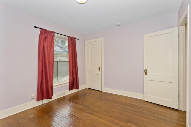 empty room with wood-type flooring, a textured ceiling, and baseboards