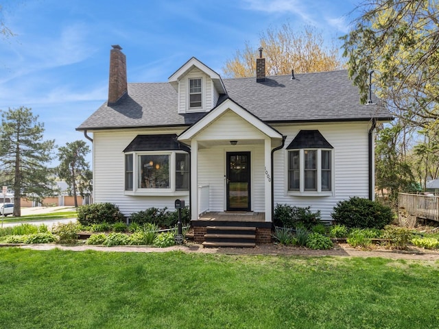 view of front of home with roof with shingles, a front yard, and a chimney