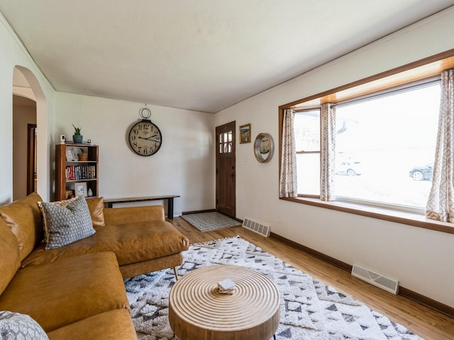 living room with arched walkways, baseboards, wood finished floors, and visible vents